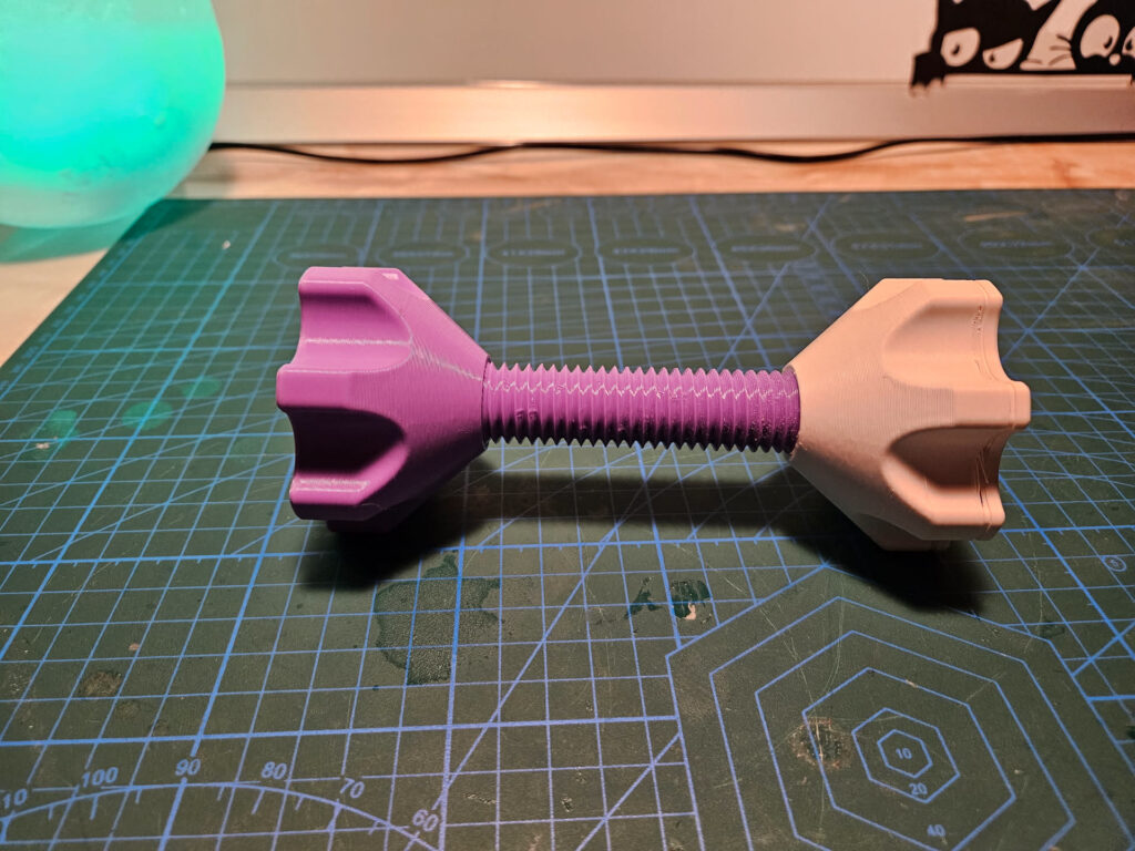 Two-colour 3D printed dumbbell with a purple printed threaded rod and beige knob on a cutting mat