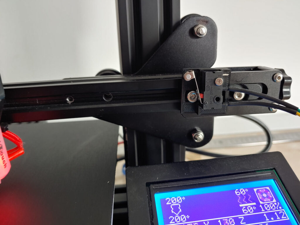 X-axis end of an Ender 3 Pro gantry with an add-on belt tensioner knob and the X endstop switch