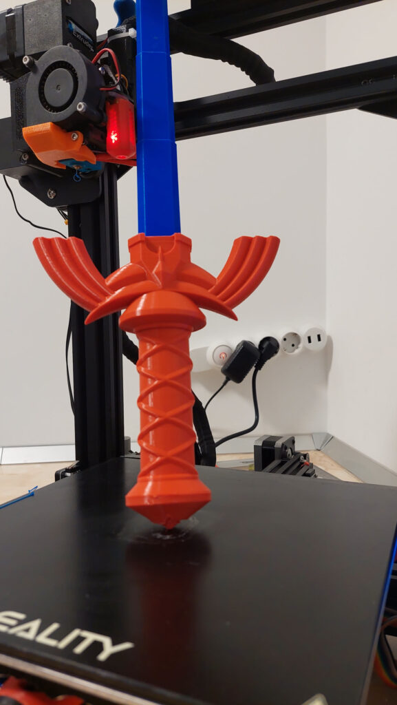 Tall red and blue sword hilt printing upright on a Creality bed slinger's moving bed