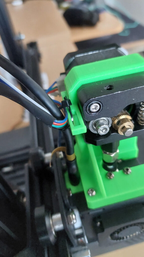 Green printed direct drive bracket carrying a metal extruder with brass drive gear above the hotend