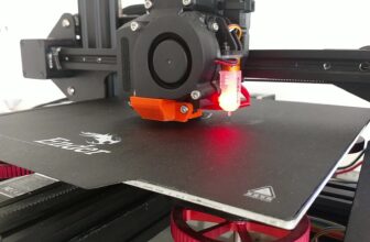 Close-up of a modded Ender 3D printer with a probe, orange printed fan duct, blower fan and red leveling knobs over the bed