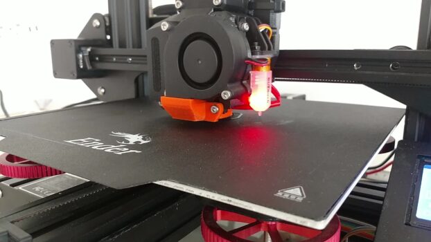 Close-up of a modded Ender 3D printer with a probe, orange printed fan duct, blower fan and red leveling knobs over the bed
