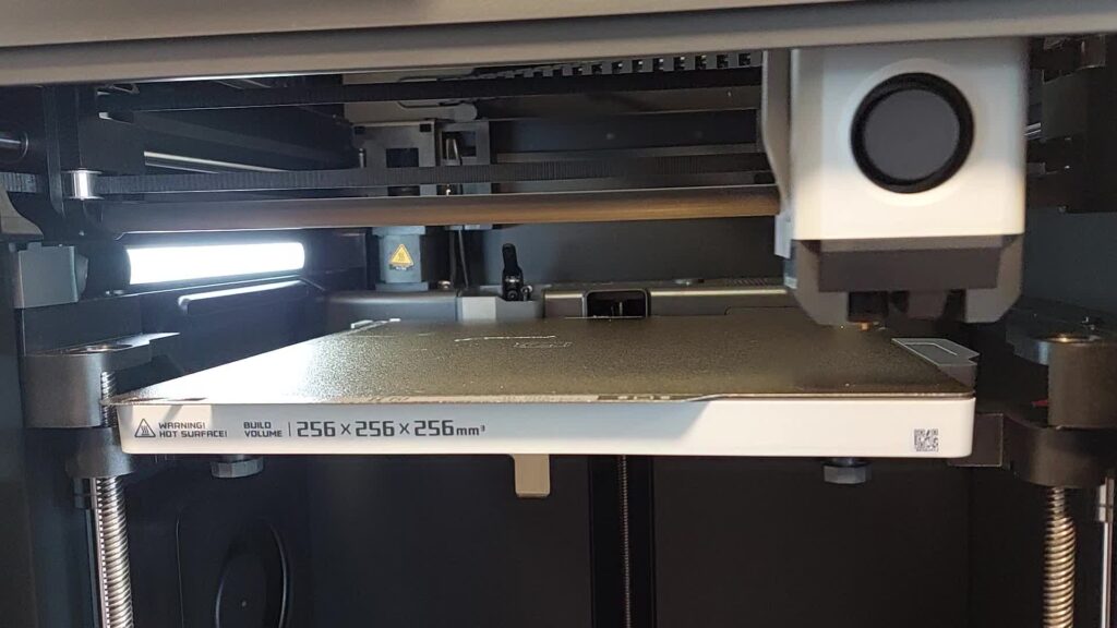 Inside an enclosed CoreXY printer: belt-driven toolhead above a build plate mounted on Z lead screws, 256 mm build volume