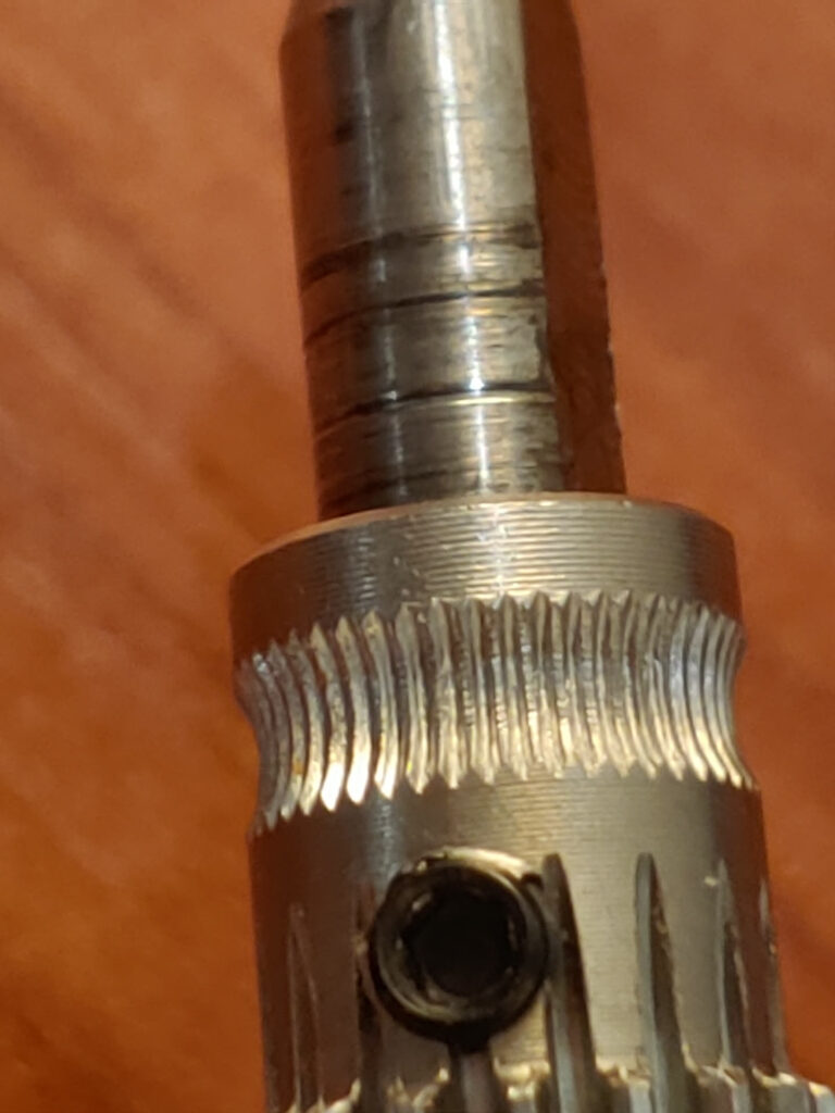 Close-up of a hobbed extruder drive gear on its motor shaft, with the set screw visible