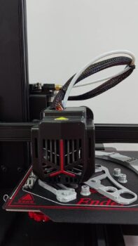 3D printer toolhead with fan shroud and braided cables, with printed wrenches and tools laid on the heated bed