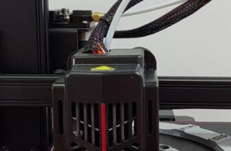 3D printer toolhead with fan shroud and braided cables, with printed wrenches and tools laid on the heated bed