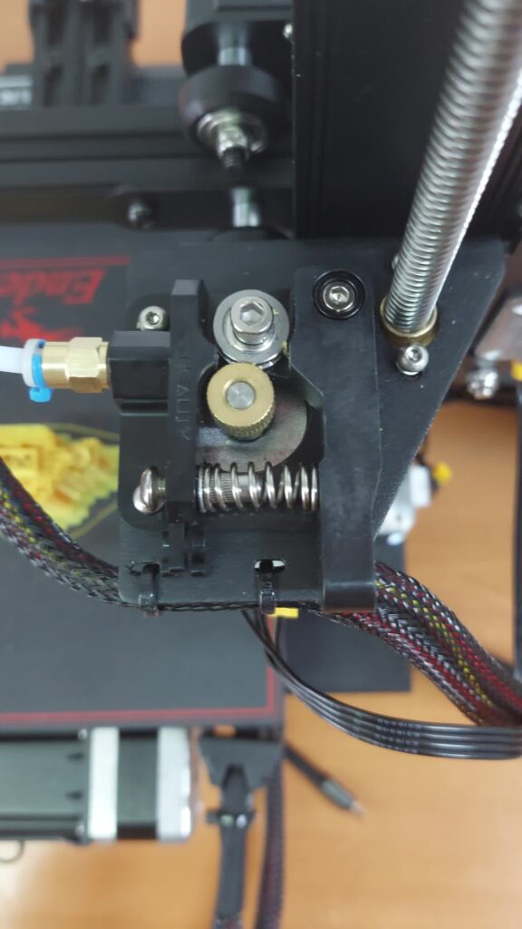 Creality Ender-style extruder with the brass drive gear, idler bearing and tension spring visible, ready for inspection