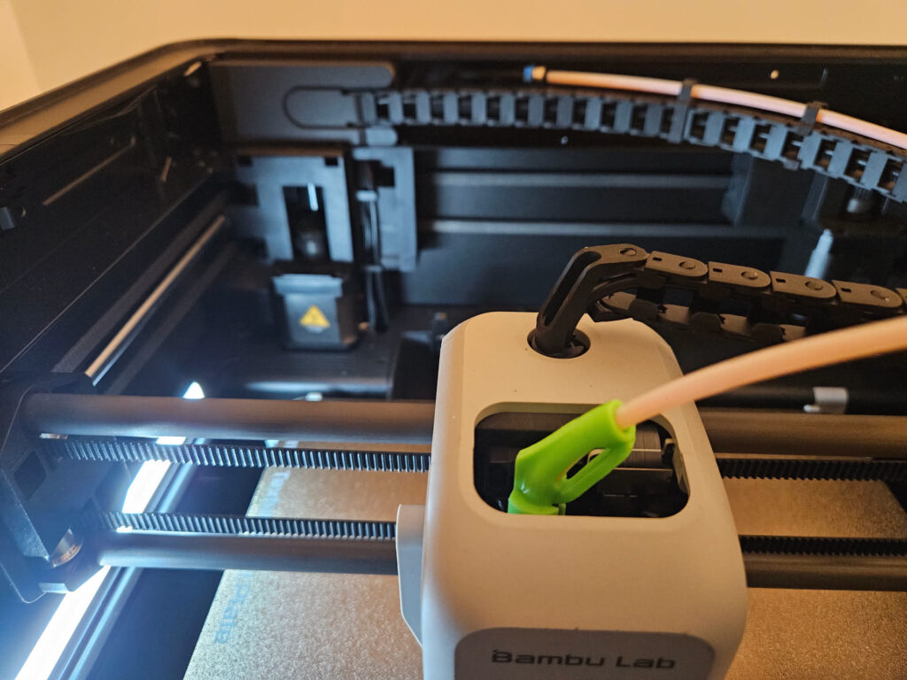 Bambu Lab P1S toolhead over the textured plate, with the cable chain and a green printed tube guide