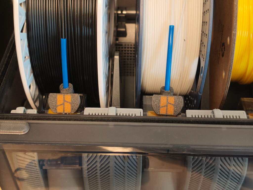 Close-up inside a Bambu Lab AMS: black and white spools feeding through printed filament guides
