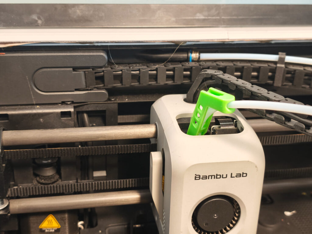 Bambu Lab P1S toolhead on its carbon rods and belts, with a green printed PTFE tube guide on top