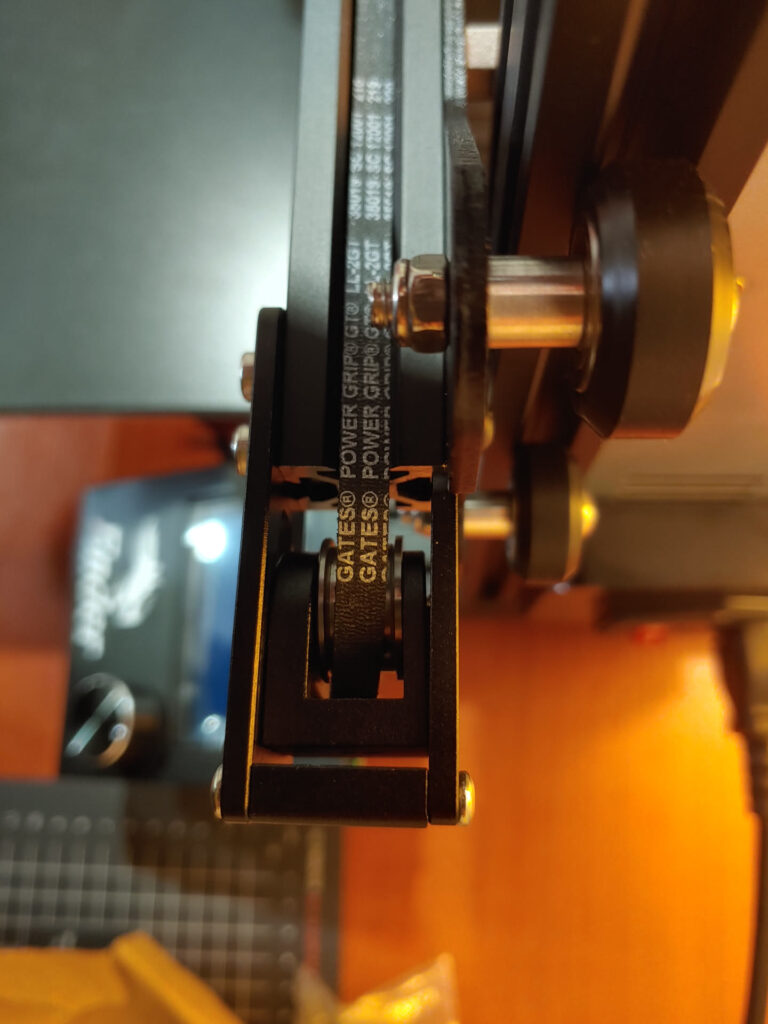 Close-up of a Gates PowerGrip GT2 belt running over a pulley inside a metal tensioner bracket at the end of an aluminium extrusion