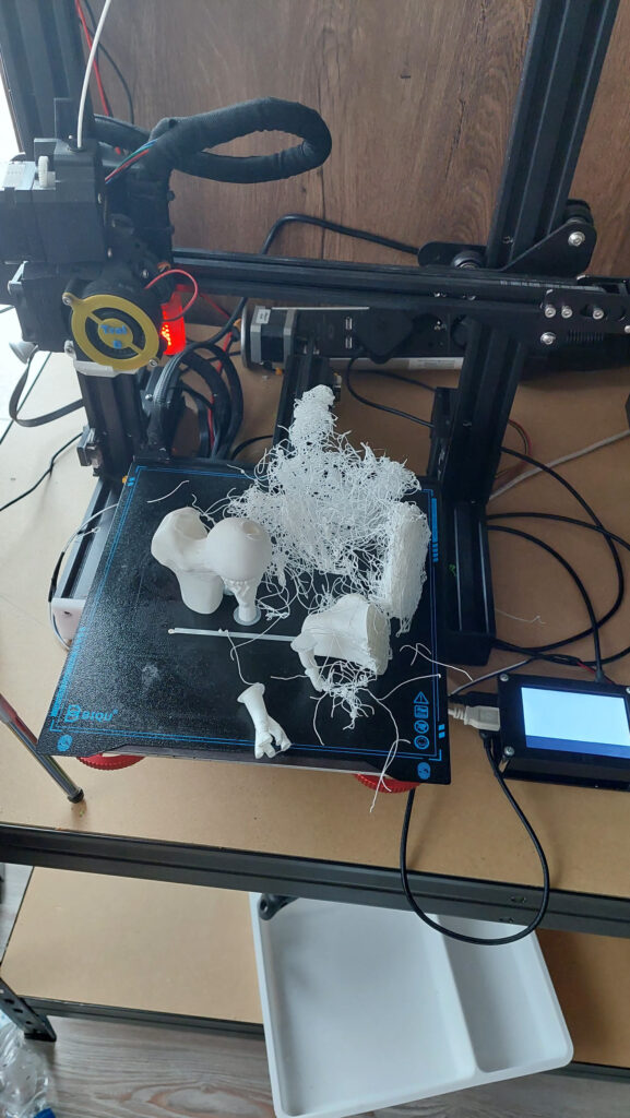 Failed print on a Biqu B1: a large tangle of white spaghetti filament across the bed next to several white bone-model parts