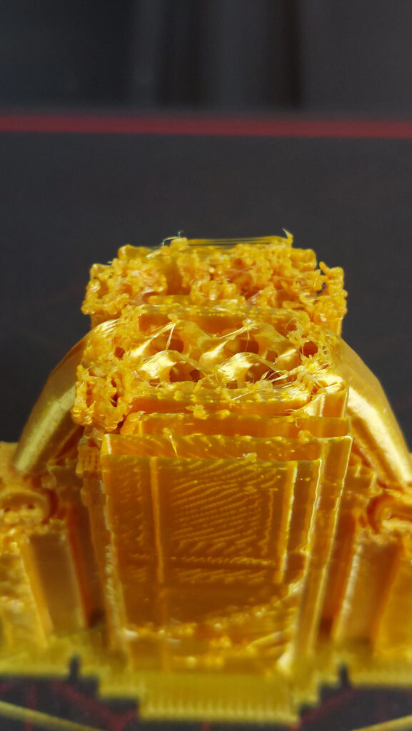 Close-up of a yellow print with rough, under-filled top layers, loose strands across the gaps and small blobs on the surface