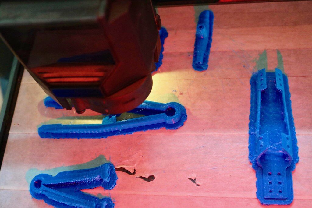 Printhead above blue FDM parts on the print bed during printing.
